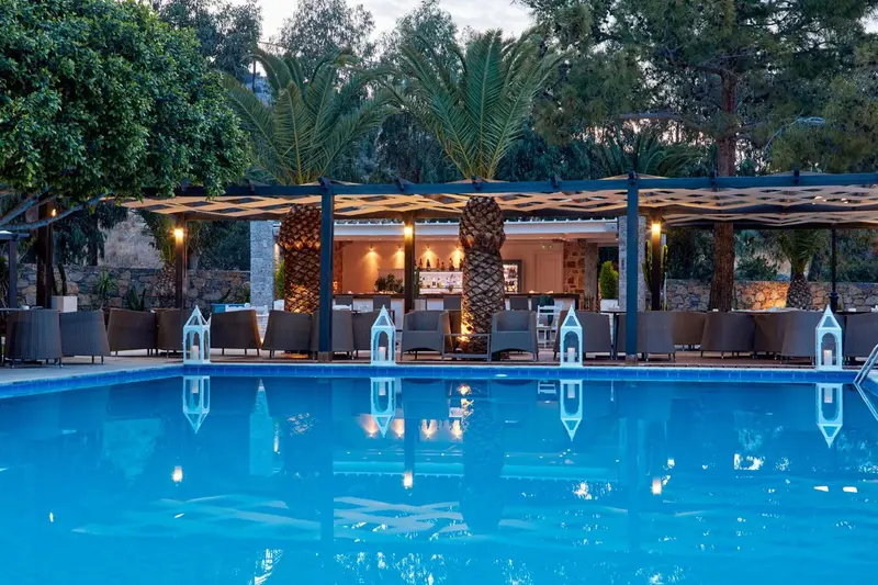 Une piscine turquoise reflète un bar éclairé dans un cadre tropical.