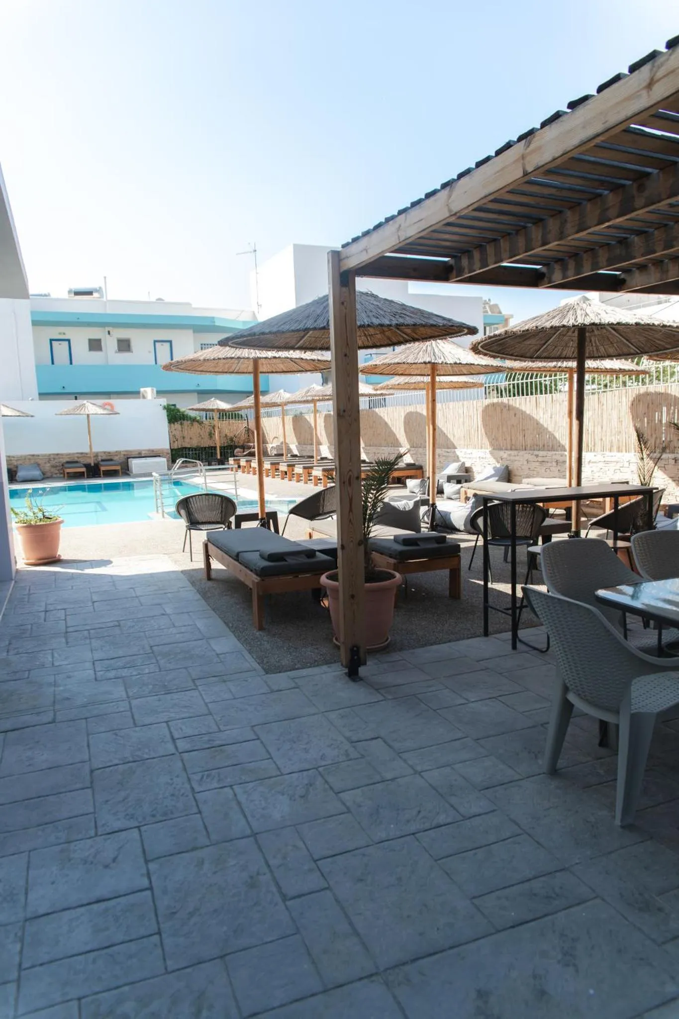 Terrasse ombragée avec transats et tables près d'une piscine.