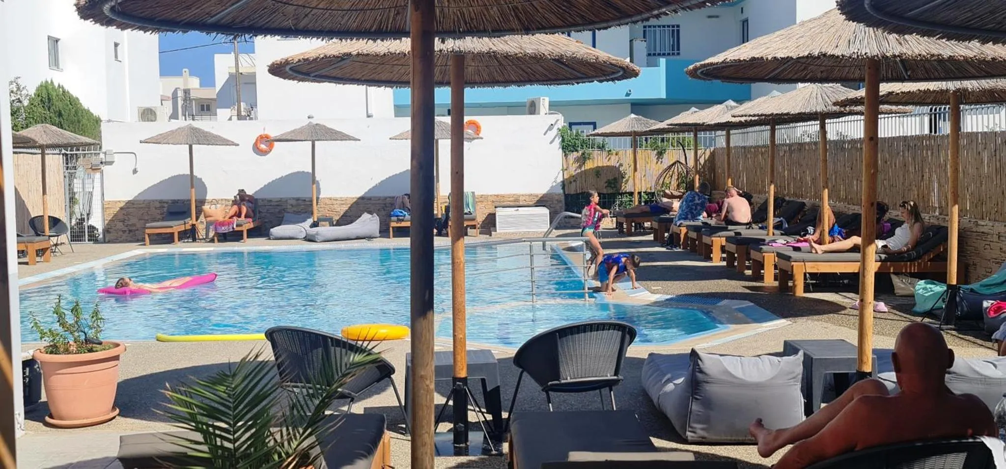 Transats et parasols ombragent une piscine avec des personnes se relaxant au soleil.