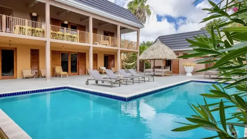 Terrasse avec chaises longues et piscine turquoise devant un bâtiment aux couleurs vives.