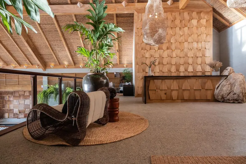 Espace de réception lumineux avec mobilier en bois et plantes tropicales.