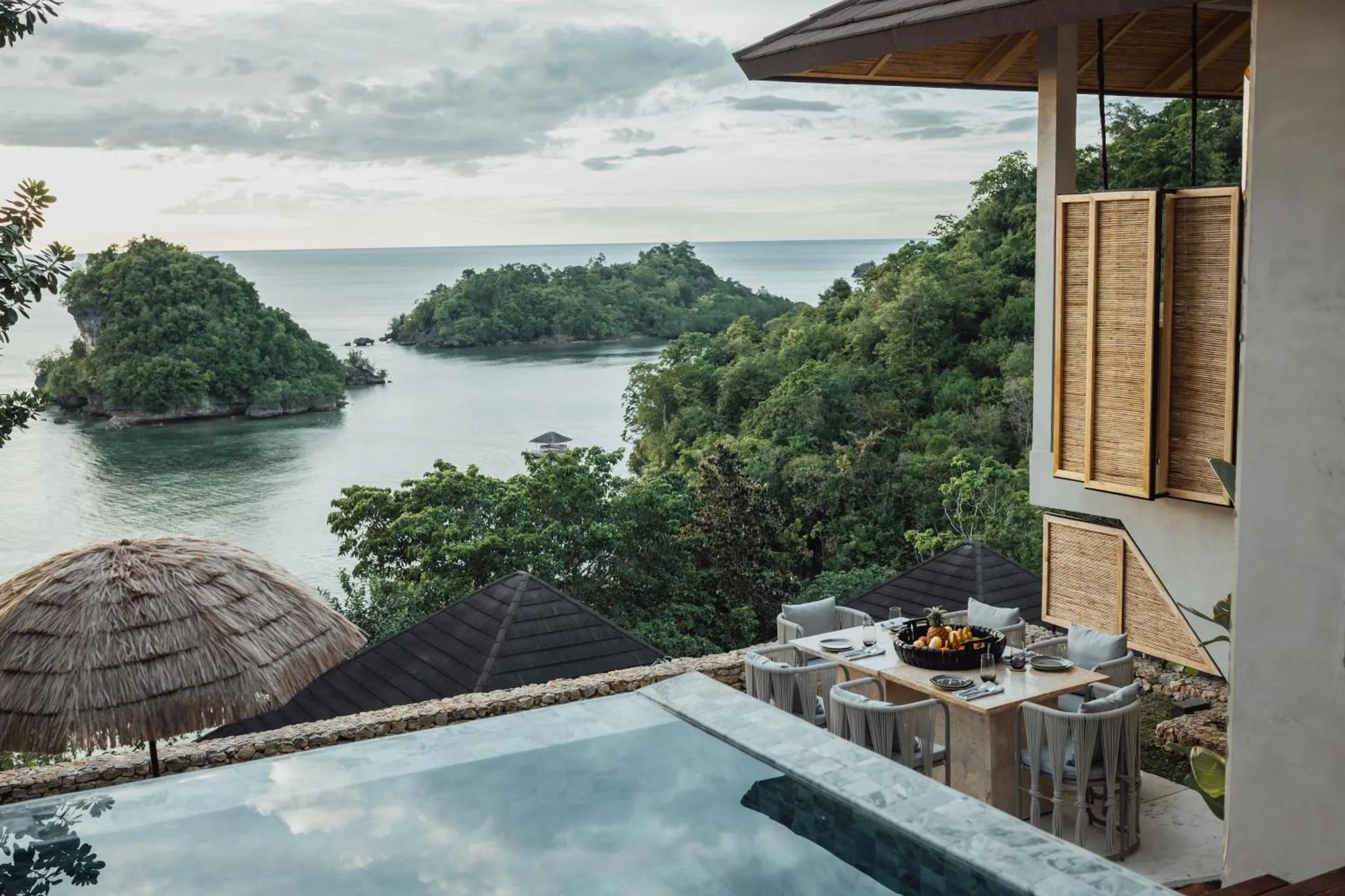 Une table à manger est mise en scène sur une terrasse avec piscine, face à une vue sur la mer et les îles.