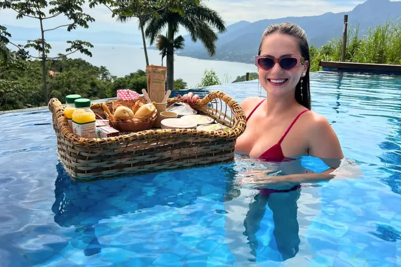 Une femme souriante profite d'un petit-déjeuner servi dans une piscine à débordement avec vue sur la mer.