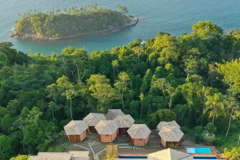 Vue aérienne de bungalows au toit de chaume entourés d'une végétation luxuriante et donnant sur la mer.
