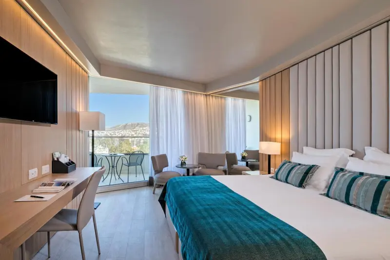 Chambre lumineuse avec un lit confortable et un espace salon ouvert sur un balcon.