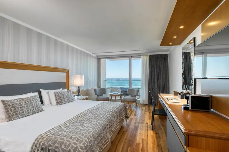 Une chambre lumineuse avec un grand lit et un balcon donnant sur la mer.