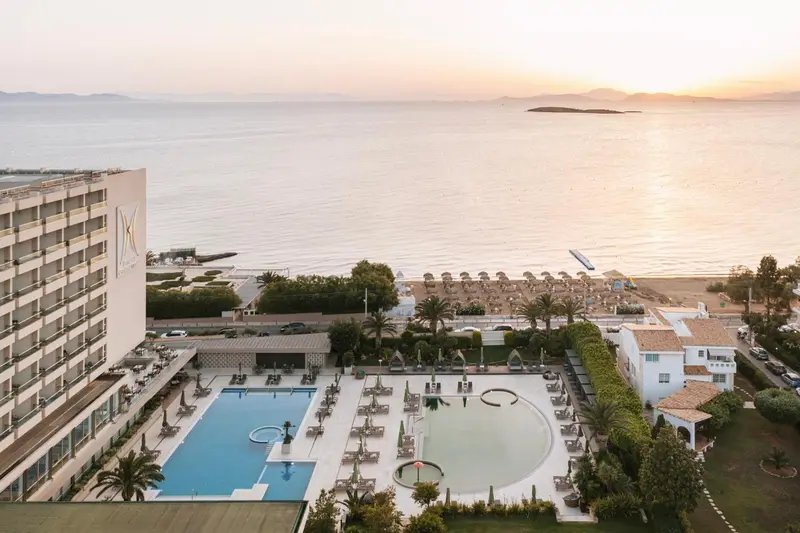 Vue aérienne d'un complexe hôtelier avec piscine et accès à la plage au coucher du soleil.