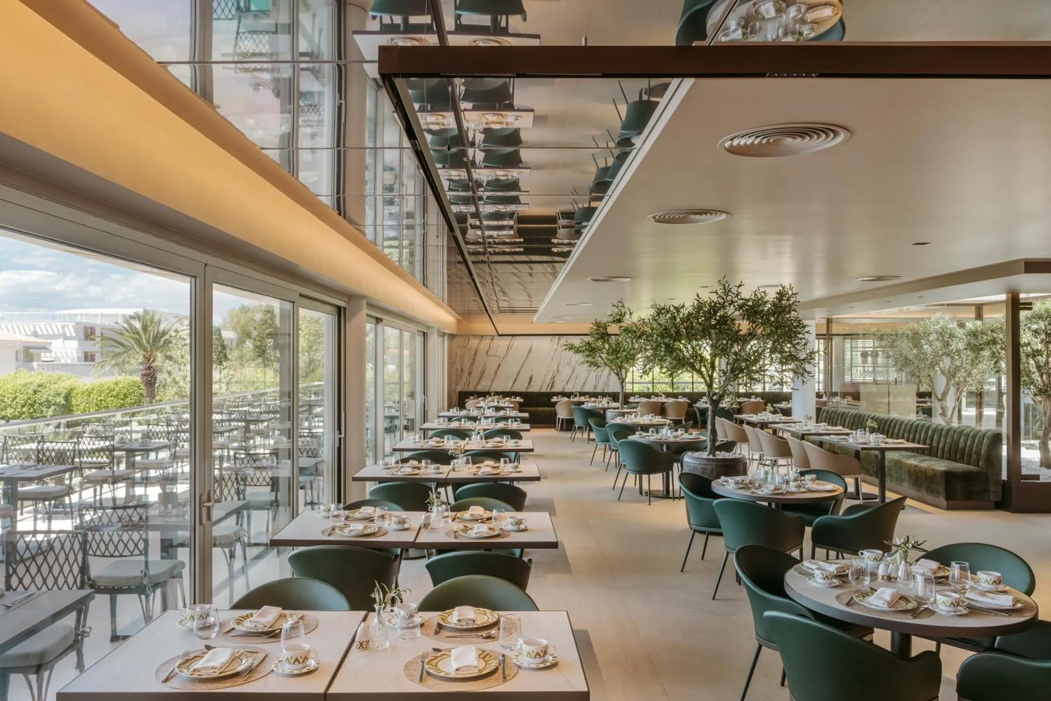 Une salle lumineuse avec des tables dressées et de grandes baies vitrées donnant sur un jardin.