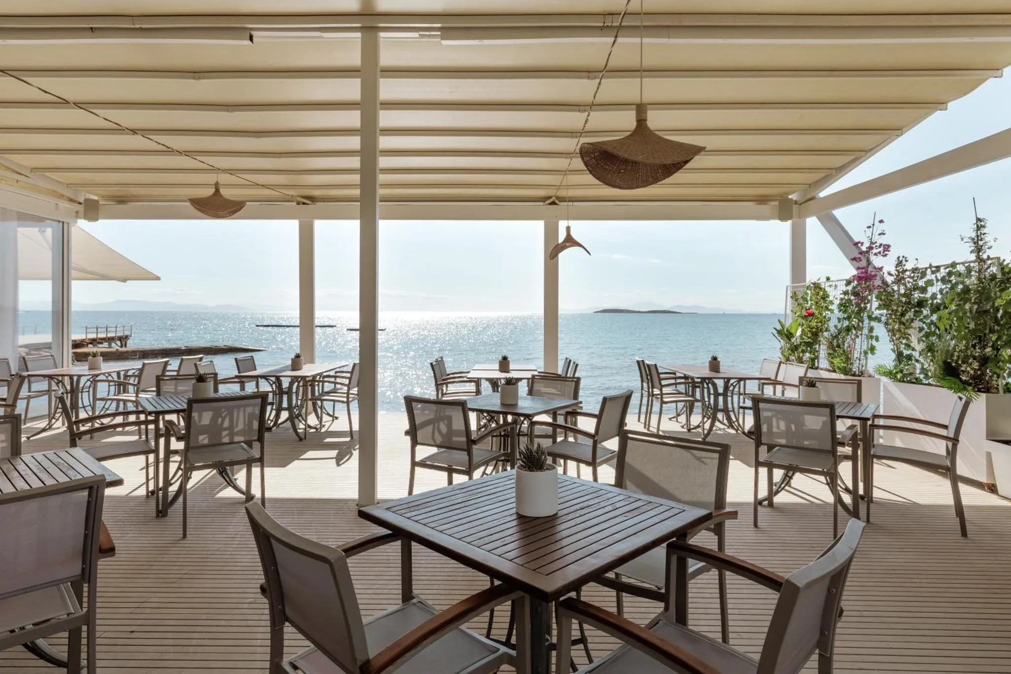 Terrasse ombragée avec tables et chaises donnant sur la mer.