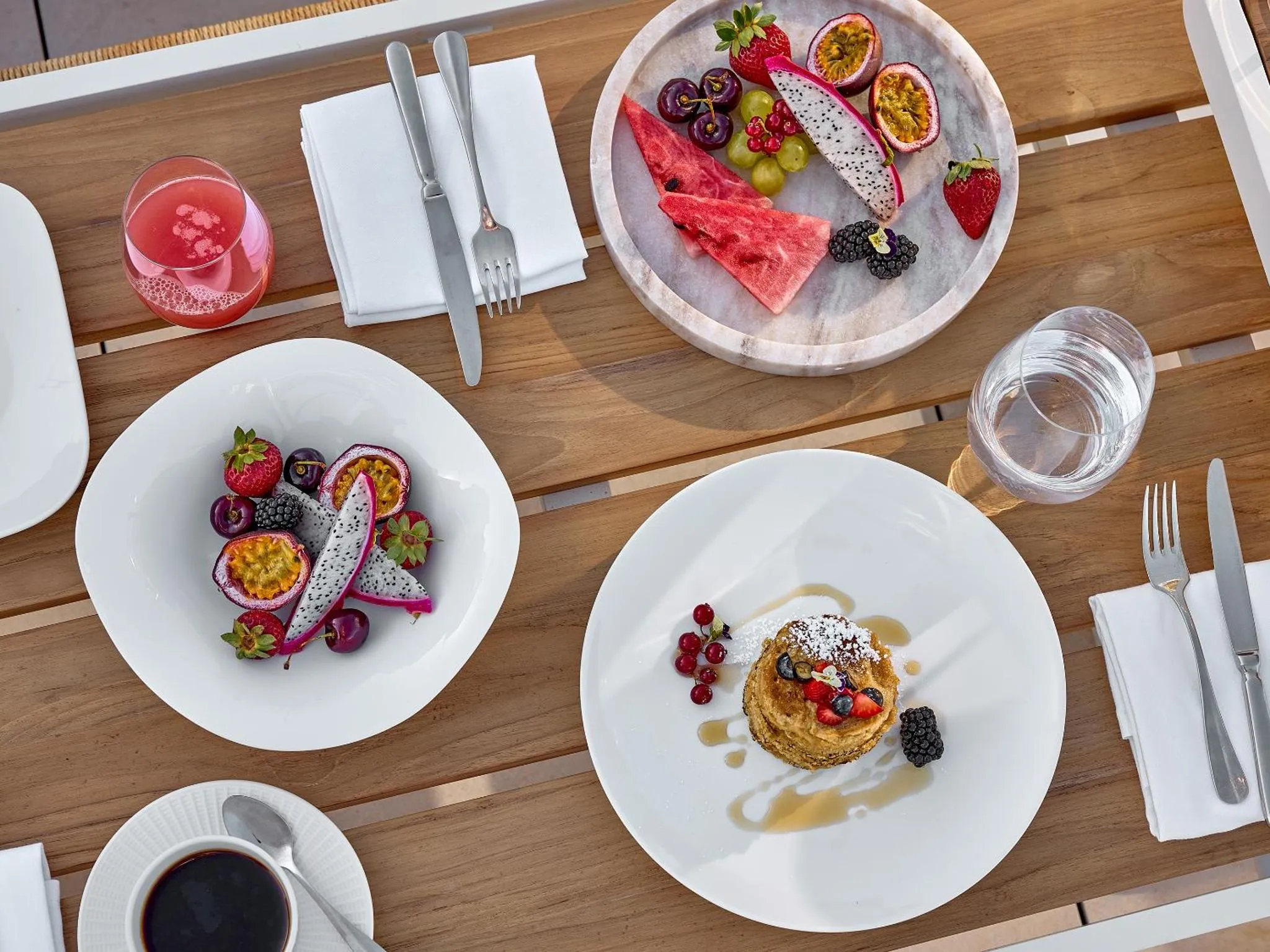 Assiettes de fruits frais et de pancakes sur une table en bois.