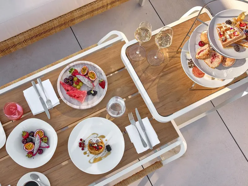 Une table est dressée avec des couverts, des assiettes de fruits et des pâtisseries.
