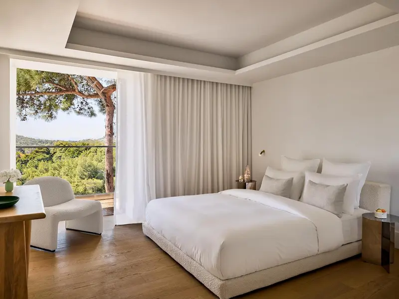 Chambre lumineuse avec un grand lit et vue sur la végétation.