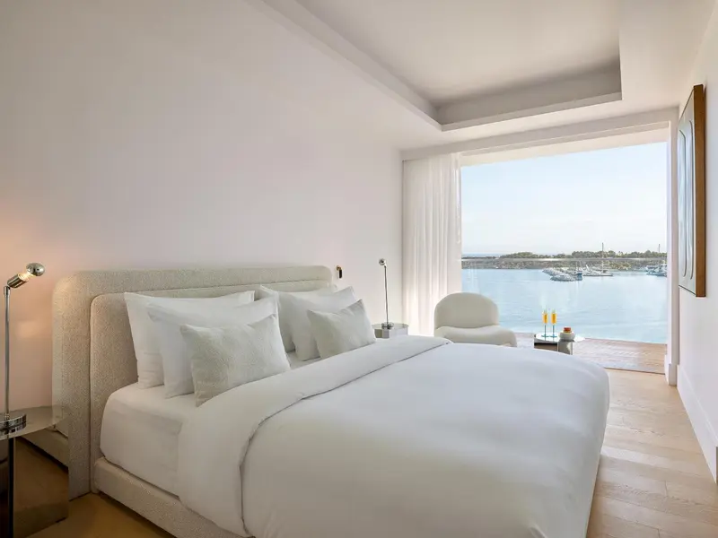 Une chambre lumineuse avec un grand lit face à une baie vitrée donnant sur la mer.