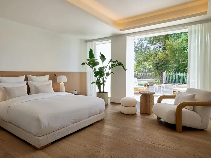 Une chambre lumineuse avec un grand lit et un coin salon donnant sur une terrasse.