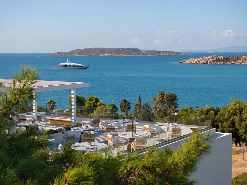 Terrasse aménagée avec tables et chaises offrant une vue sur la mer et une île.