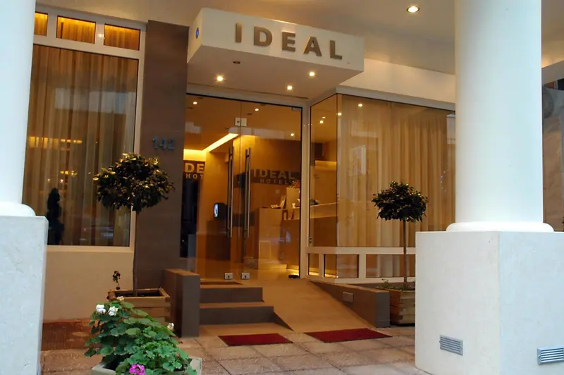 Entrée d'un hôtel avec un auvent vitré et des arbustes décoratifs.