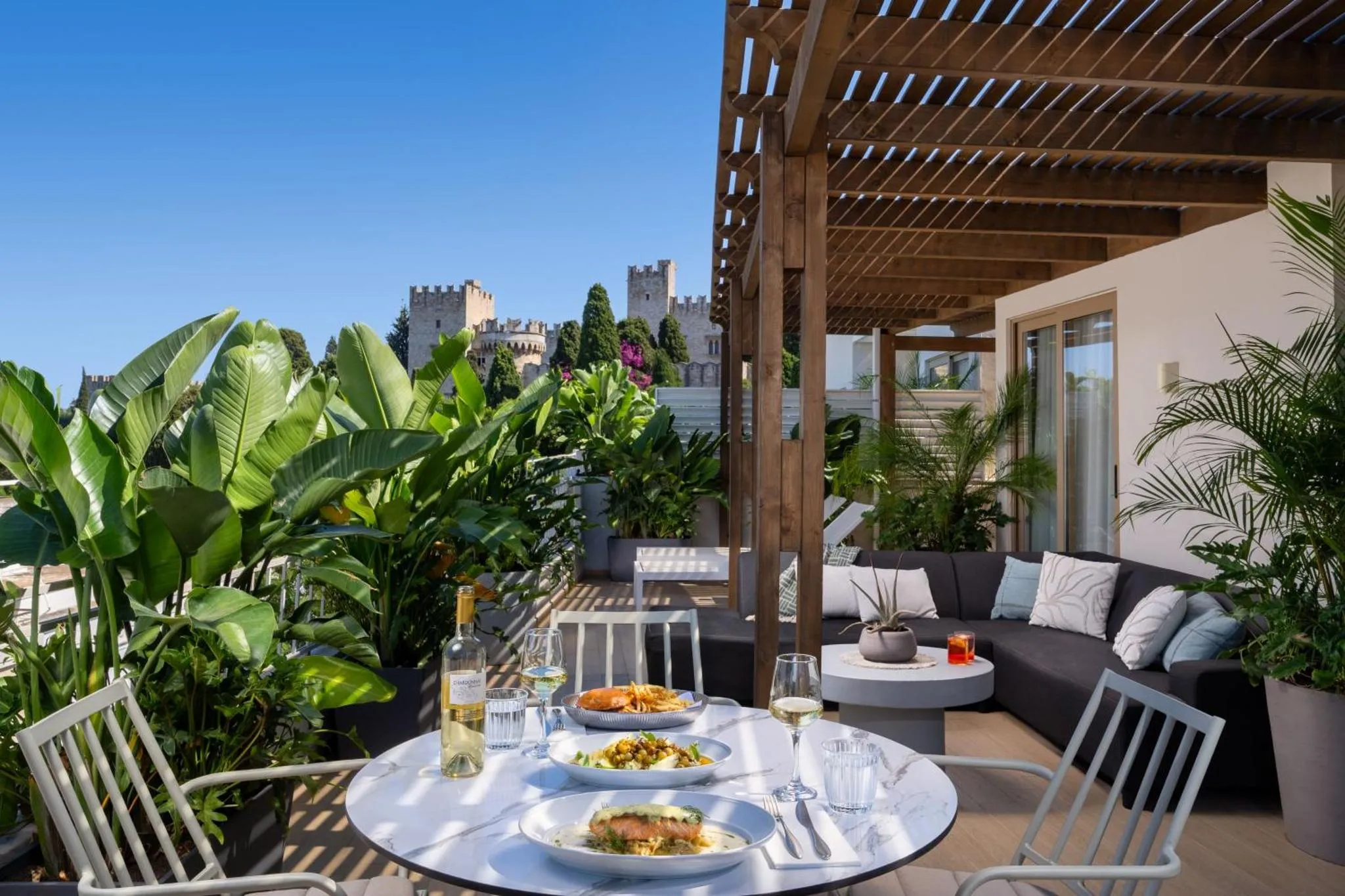 Une table est dressée avec des plats et des boissons sur une terrasse ombragée.