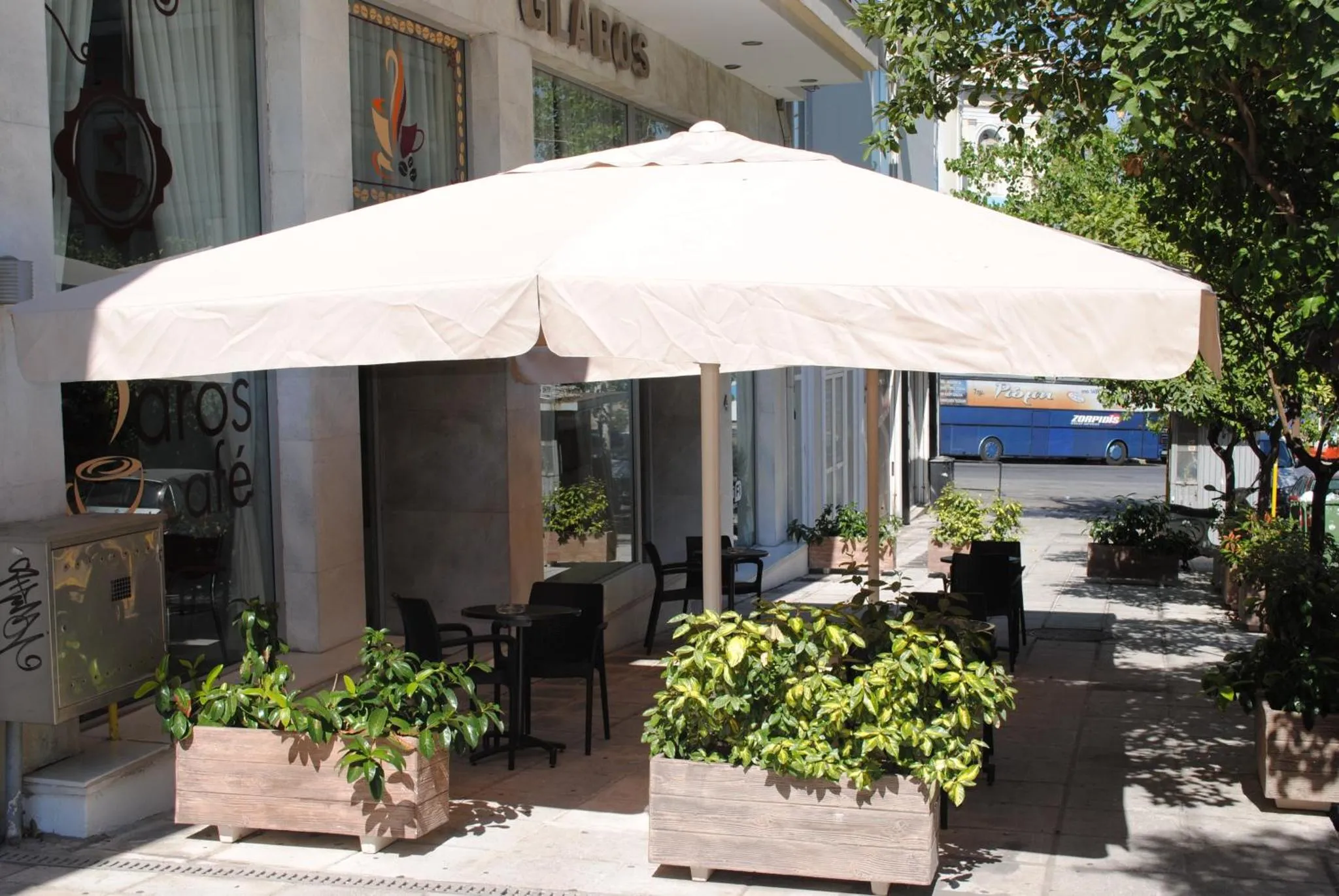 Terrasse ombragée avec tables et plantes en pots devant un café.