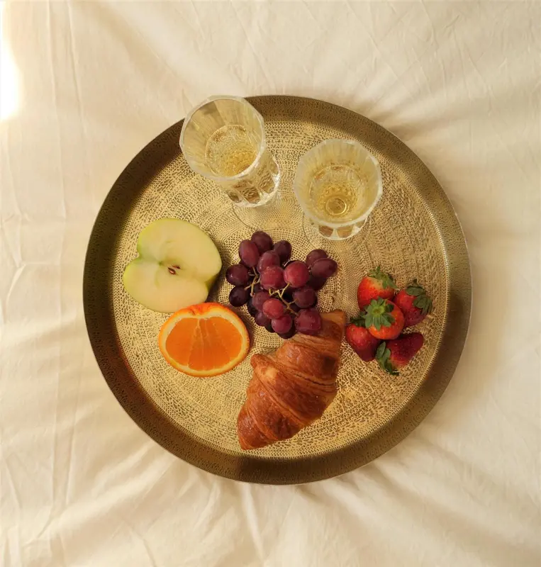 Un plateau doré présente des fruits frais, une viennoiserie et des boissons.