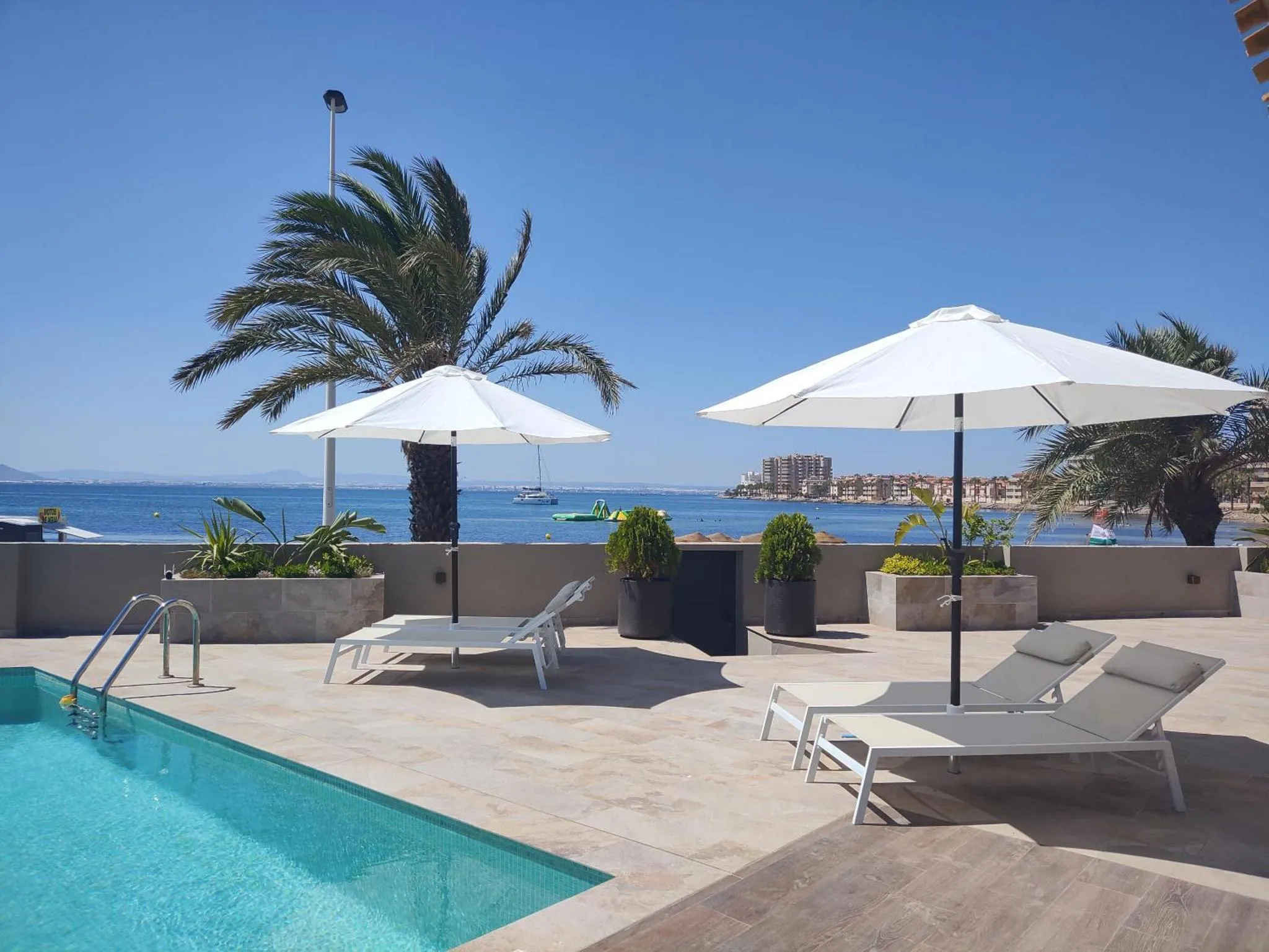 Terrasse avec transats et parasols au bord d'une piscine, vue sur la mer.