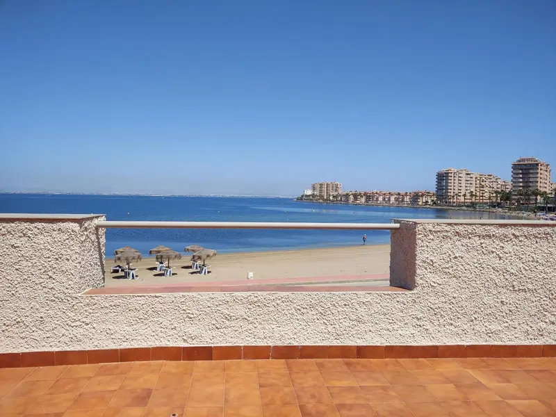 Vue sur la mer et la plage depuis un balcon ensoleillé.