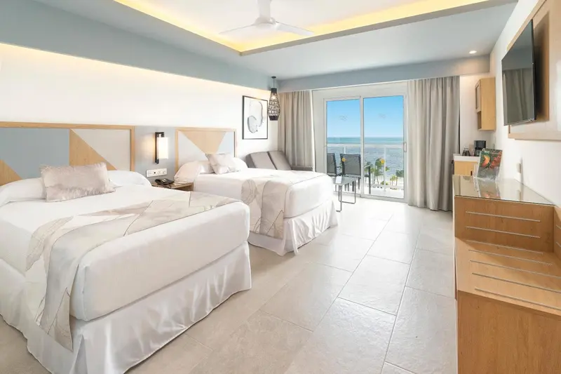 Chambre lumineuse avec deux lits et vue sur la mer.