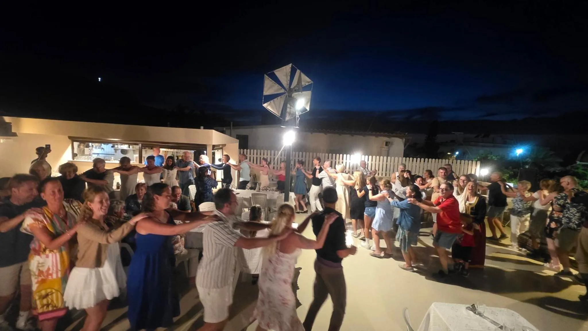 Une foule de personnes danse sur une terrasse éclairée la nuit.