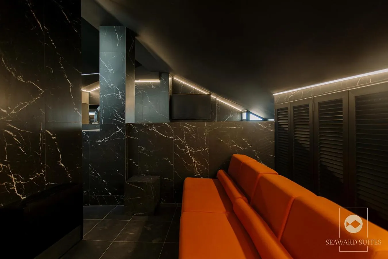Un espace de détente intérieur avec un canapé orange et des murs recouverts de marbre noir.