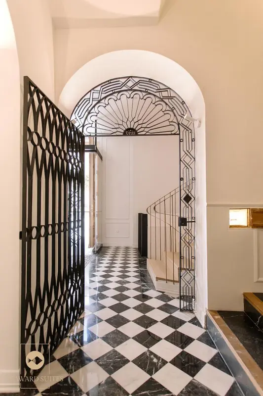 Un couloir d'hôtel avec un sol à carreaux et une porte arquée en fer forgé.