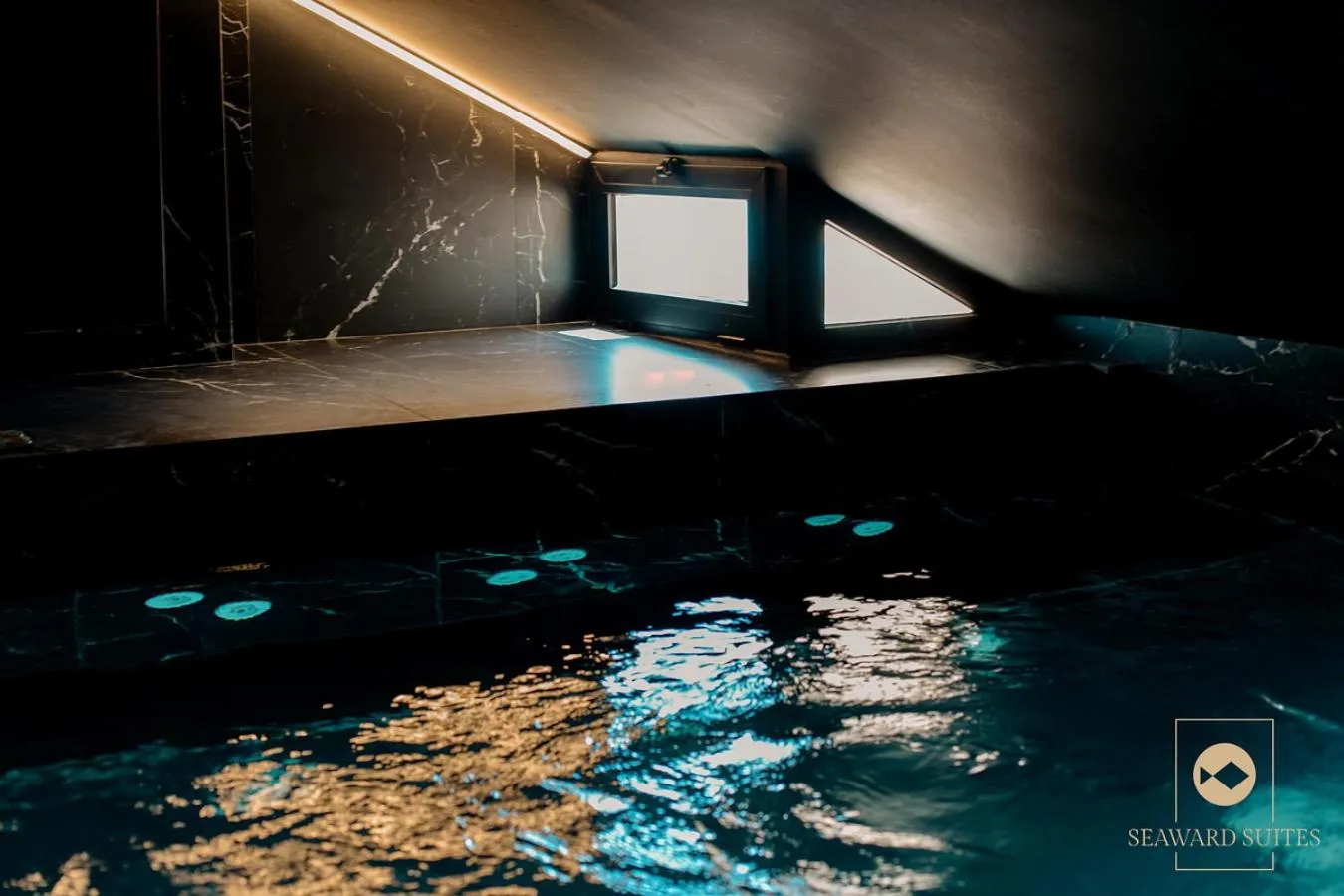 Une piscine intérieure sombre reflète des lumières dorées.