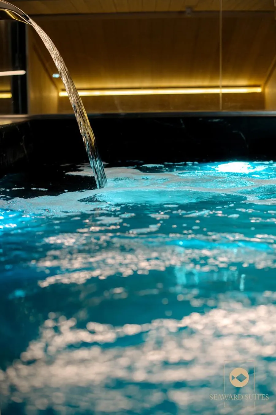 Un jet d'eau se déverse dans une piscine sombre aux reflets turquoise.