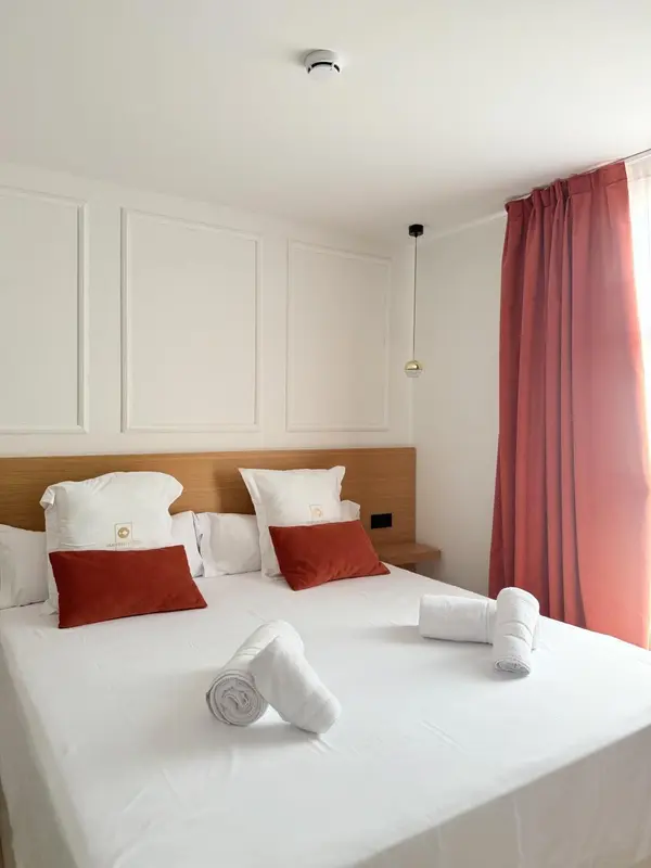Une chambre lumineuse avec un grand lit recouvert de draps blancs et d'oreillers décorés.