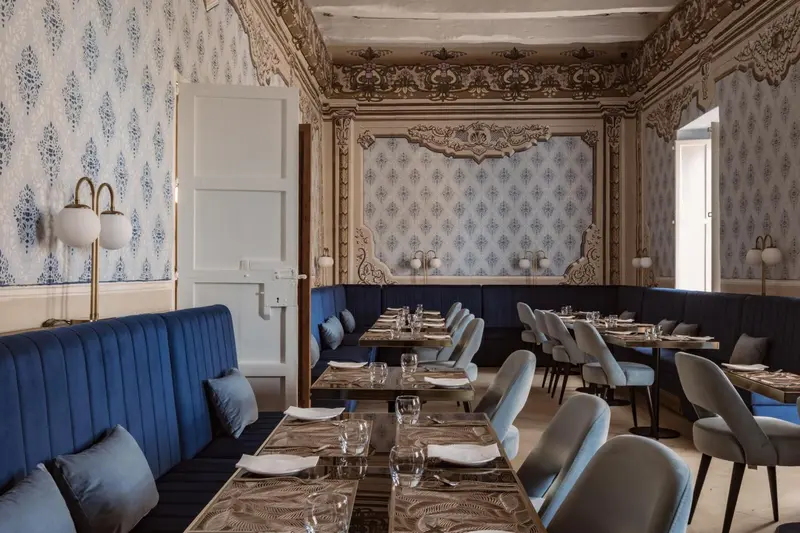 Une salle de restaurant élégante avec des tables dressées et des banquettes bleues.