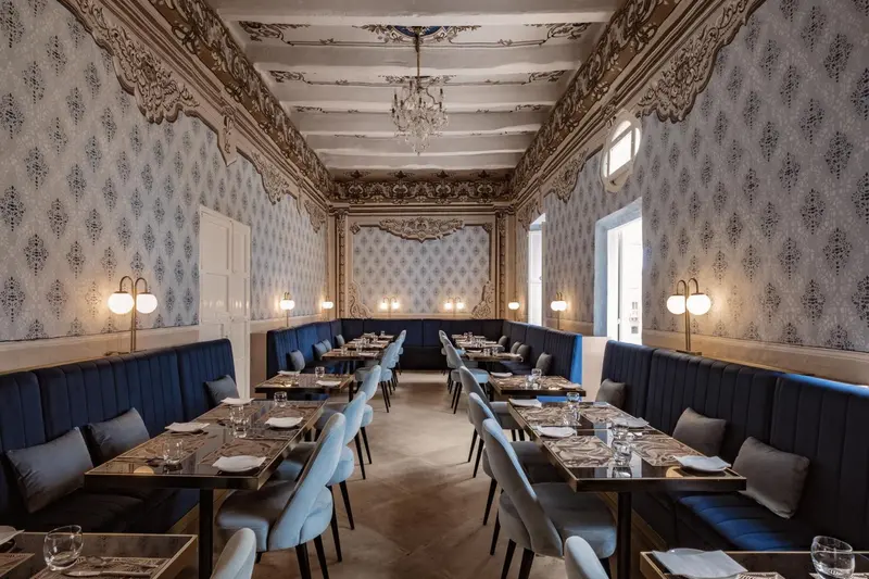 Une salle de restaurant élégante avec des tables dressées et des banquettes bleues.