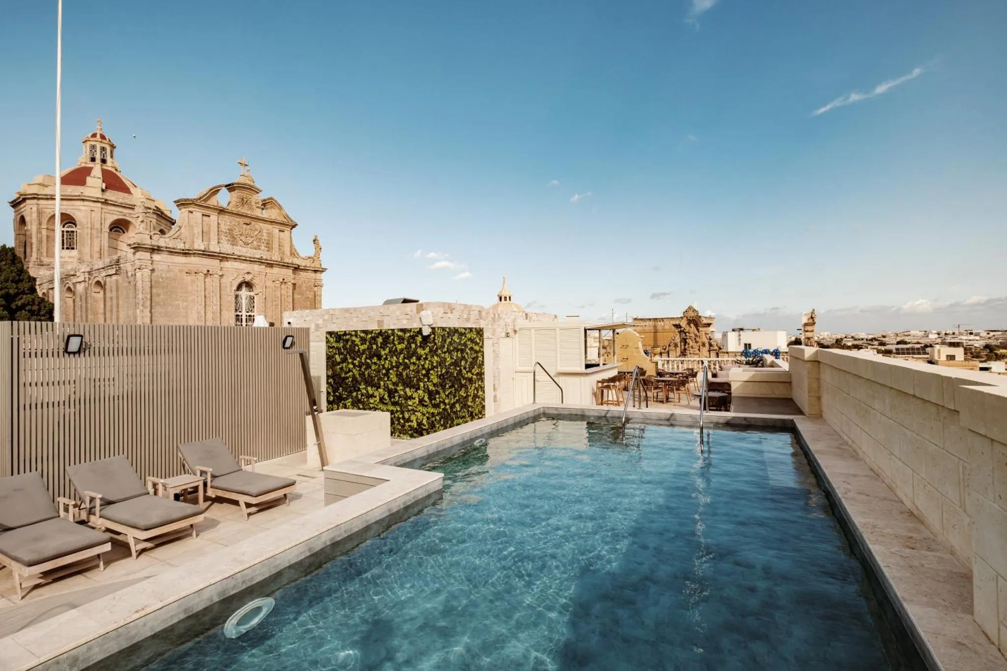 Une piscine rectangulaire sur un toit-terrasse avec des chaises longues et une vue sur la ville.
