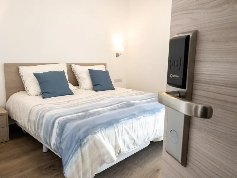 Une chambre lumineuse avec un grand lit recouvert d'une courtepointe blanche et de coussins bleus.