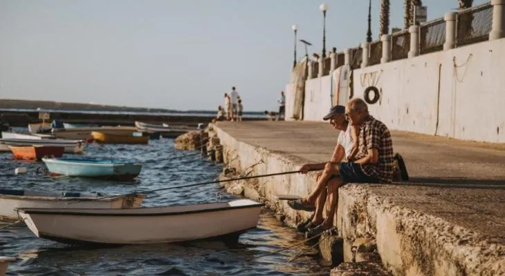 Deux hommes sont assis sur un quai et pêchent dans une eau calme.
