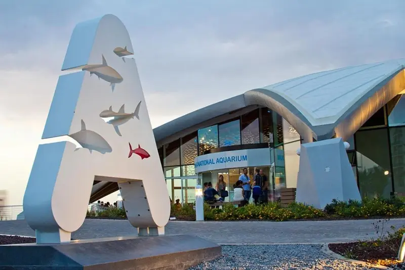 Façade d'un bâtiment moderne avec une sculpture en forme de lettre et des personnes devant.