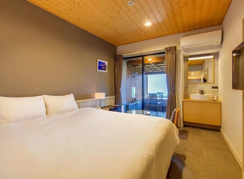Une chambre lumineuse avec un grand lit et une terrasse accessible par des baies vitrées.