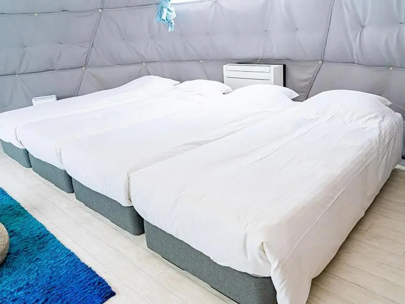 Une chambre lumineuse avec trois lits simples recouverts de draps blancs.