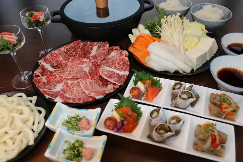 Table garnie de divers plats japonais, notamment de la viande, des légumes et des fruits de mer.