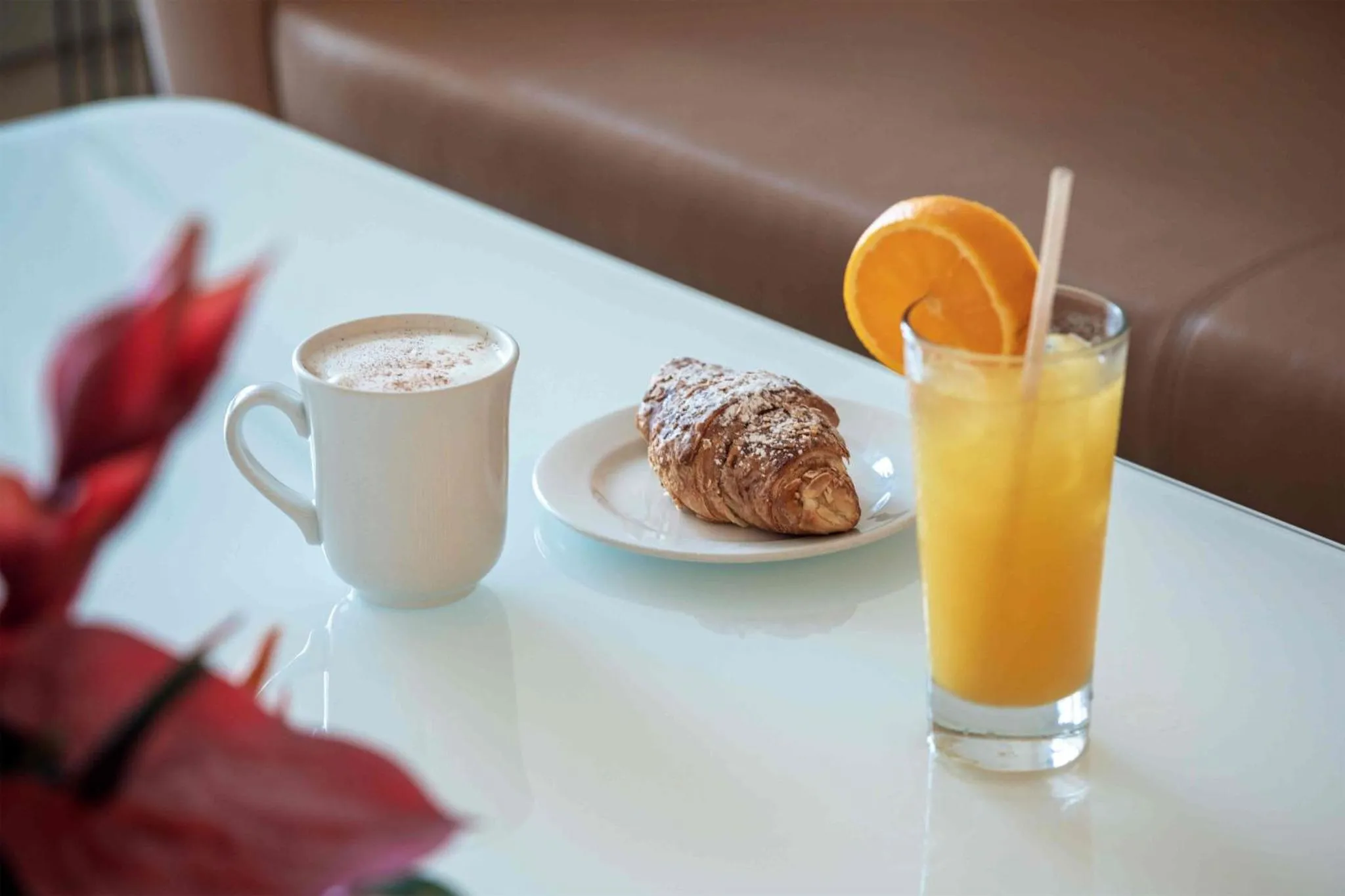 Une table blanche présente un petit-déjeuner avec un croissant, une tasse de café et un jus d'orange.