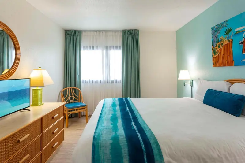 Chambre lumineuse avec un lit recouvert d'une courtepointe bleue et une commode en bois.