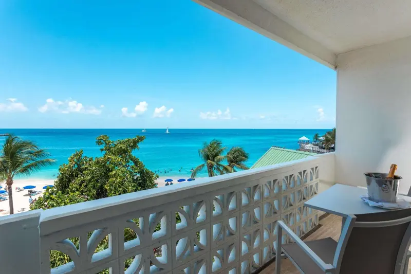 Vue sur une plage de sable blanc et une mer turquoise depuis un balcon.