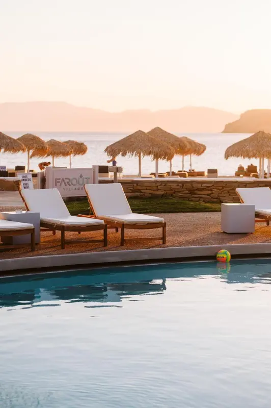 Transats blancs alignés au bord d'une piscine turquoise face à la mer.