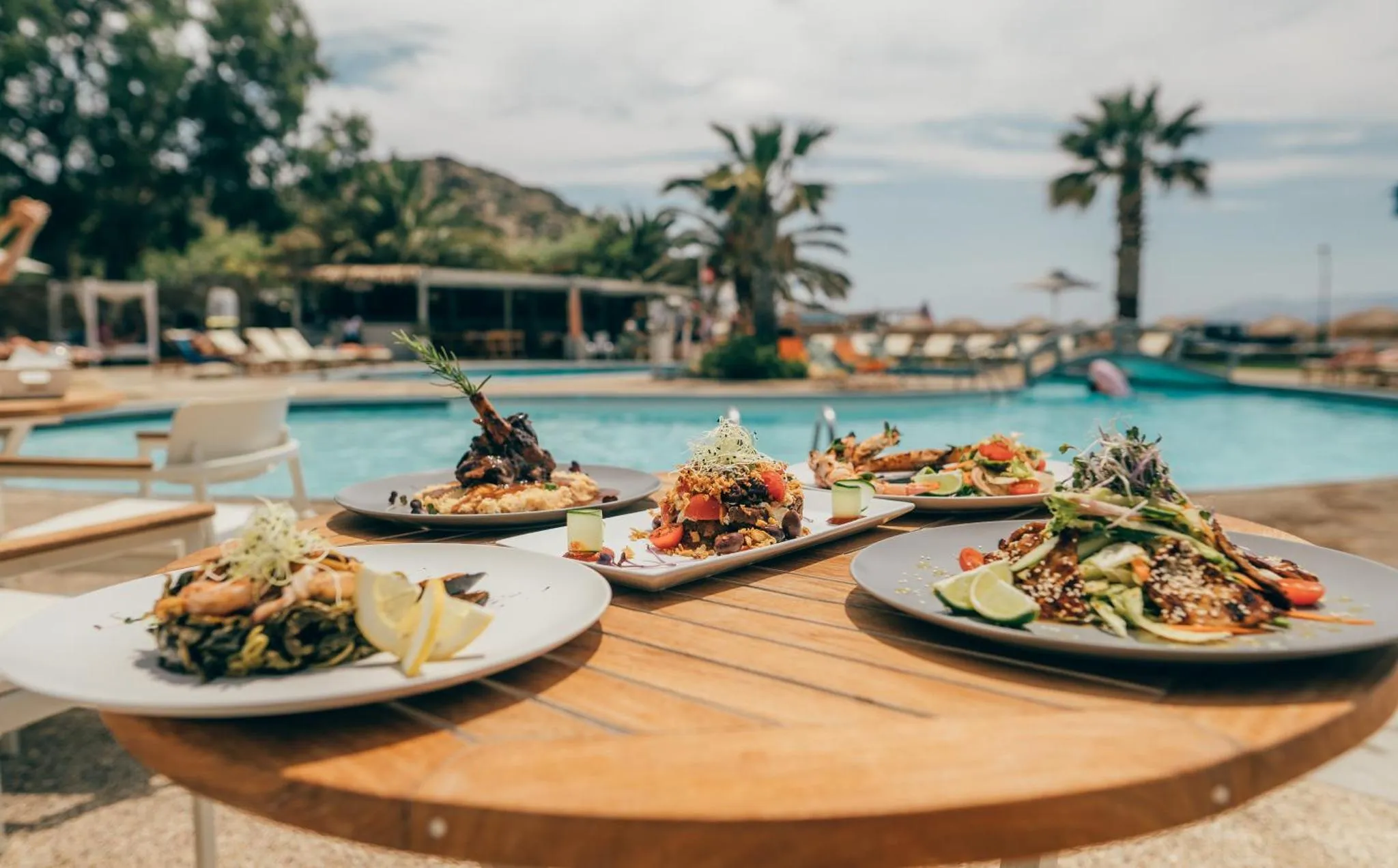 Assiettes de plats raffinés présentées sur une table en bois près d'une piscine.