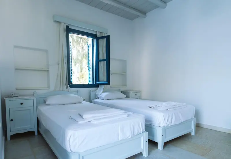 Une chambre lumineuse avec deux lits simples et une fenêtre ouverte.