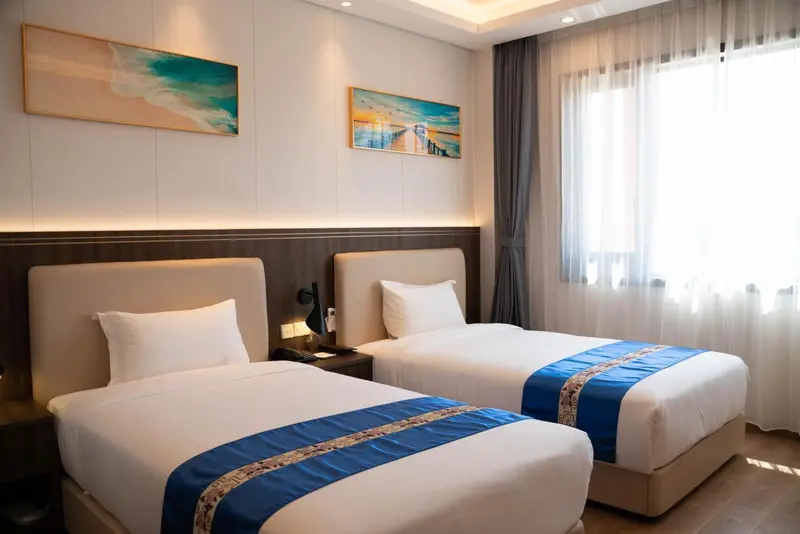 Chambre lumineuse avec deux lits simples et décoration murale.
