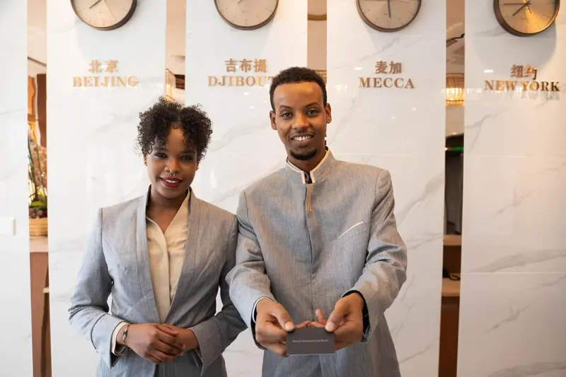 Deux employés souriants se tiennent derrière un comptoir d'accueil.