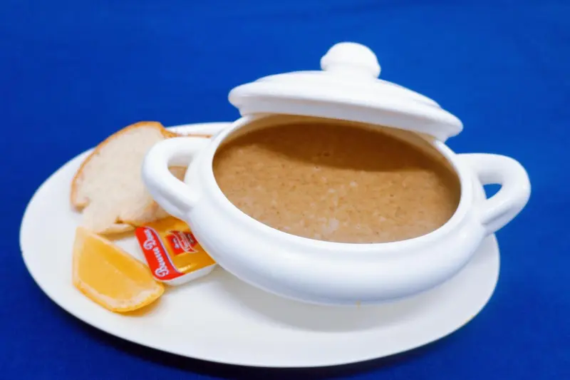 Une soupe fumante servie dans un bol blanc avec des tranches de pain et un quartier de citron.